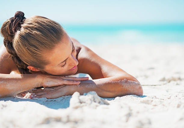 Happy woman in swimsuit relaxing while laying on sandy beach Happy young woman in swimsuit relaxing while laying on sandy beach sunbathing stock pictures, royalty-free photos & images