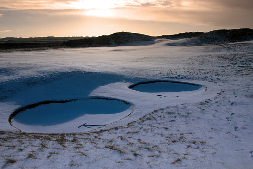 rakes in bunkers on a snow covered links golf course in ireland at sundown in snowy winter weather
