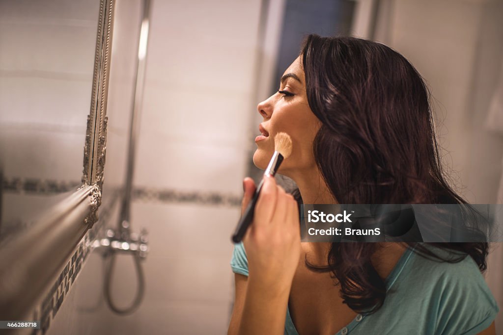 Applying face powder. Sensual young woman putting make-up in the bathroom and looking at the mirror. 2015 Stock Photo