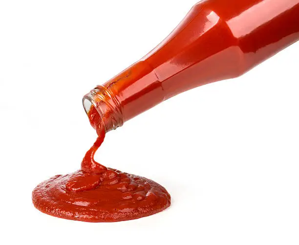 ketchup pouring out of bottle on white background