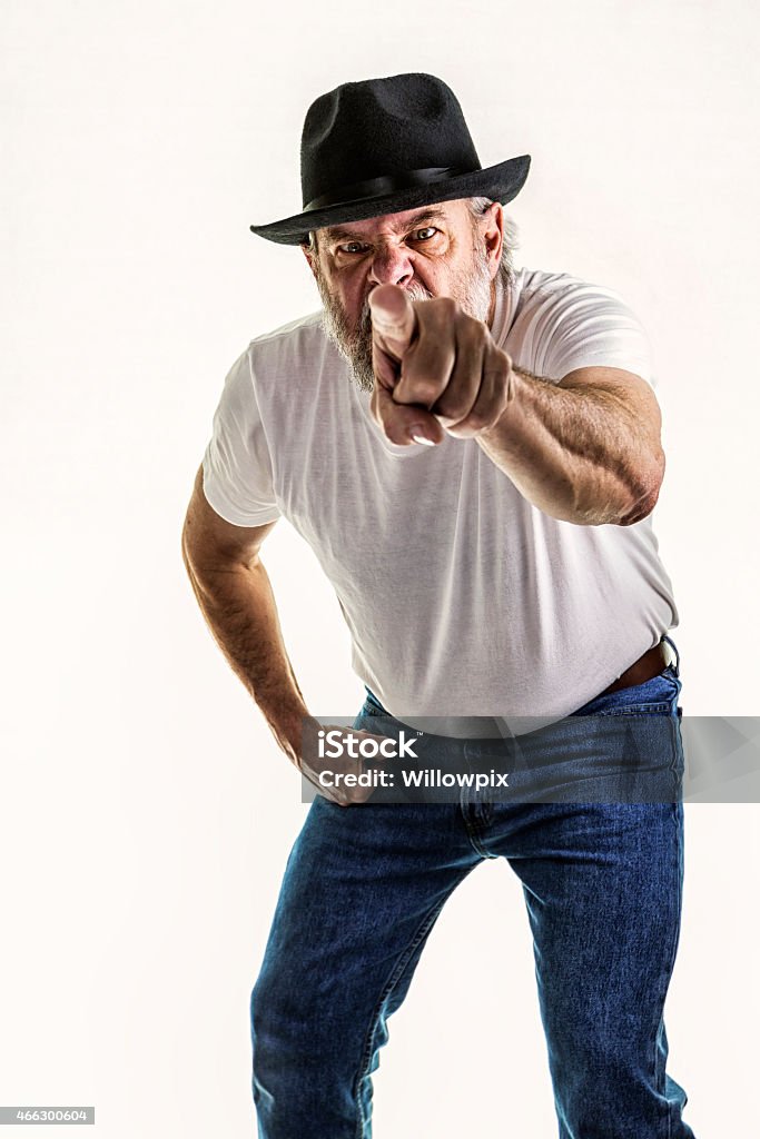 Snarling Senior Man Pointing and Threatening A snarling, threatening, grimacing senior adult man with a gray beard and mustache is pointing at the camera - apparently looking for a fight. He is wearing a white t-shirt, blue jeans, and a battered black fedora style hat. 2015 Stock Photo