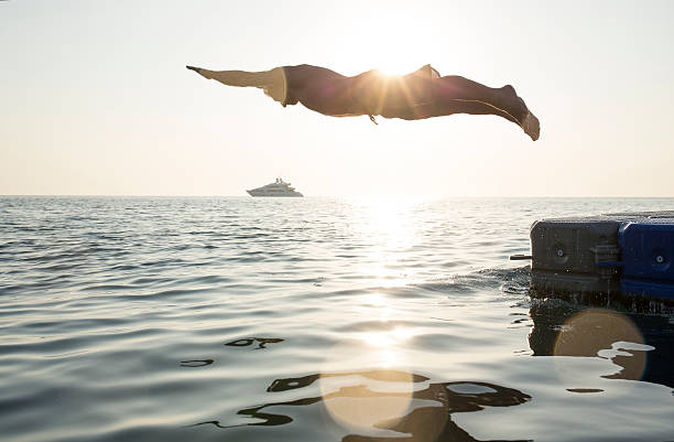 istock Man dives into tranquil sea, from pier, boat 466307136