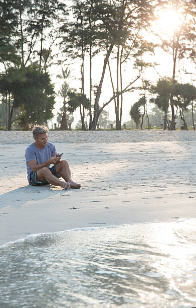 istock Man relaxes on beach, sends text on smart phone 466308620