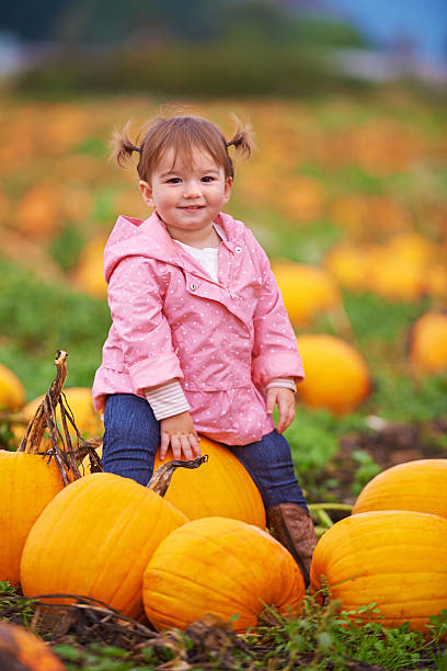 Shot of a cute little girl sitting on a pumpkin while smiling at the camera
