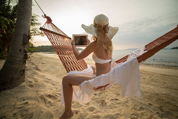 istock Woman on beach sitting on hammock using digital tablet 466315308