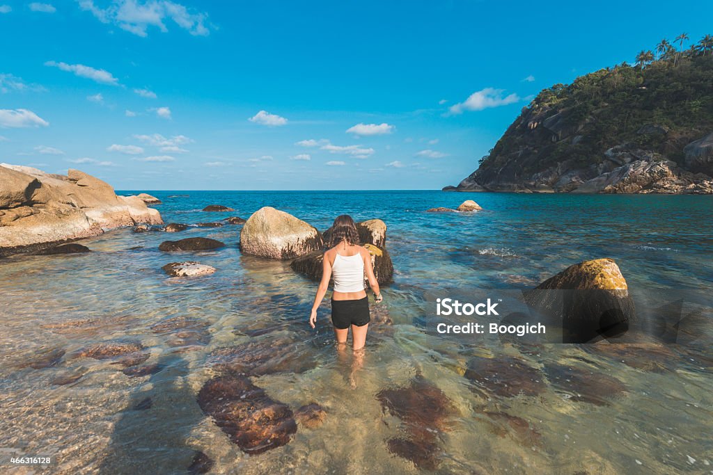 Woman Walks Into Exotic Ocean in Thailand A radiant, young American woman in her 20s walks into the water at a beach in Koh Phangan, Thailand. Surrounded by water her back is towards the camera. Photographed with a Nikon D800. 20-29 Years Stock Photo