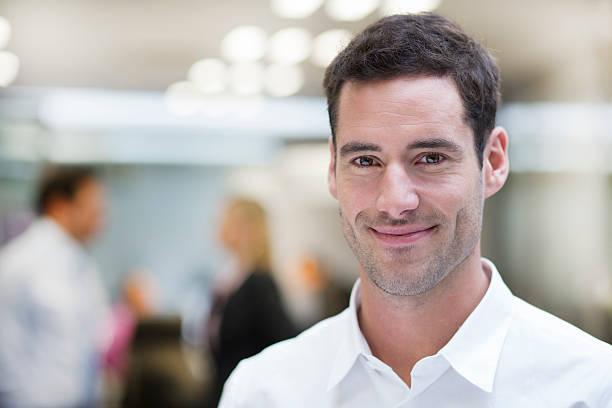 istock Smiling Businessman posing while colleagues talking together in background 466316967
