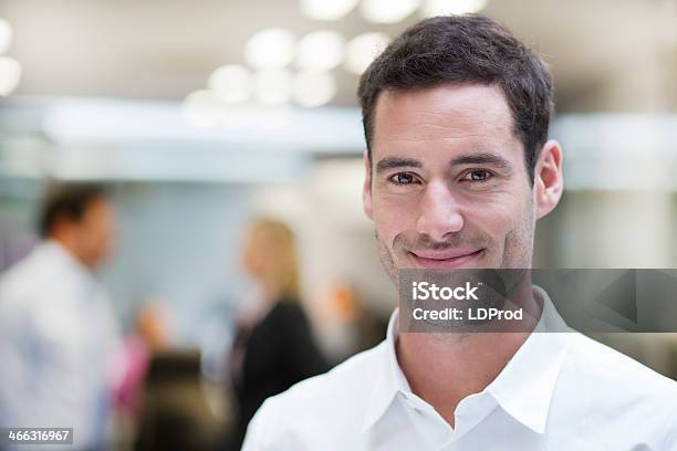 Smiling Businessman Posing While Colleagues Talking Together In Background Stock Photo - Download Image Now
