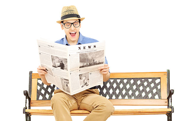 istock Excited young man reading a newspaper seated on bench 466320085
