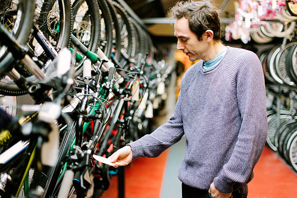 Customer in a bicycle shop, looking at the price tag Customer in a bicycle shop, smiling and looking at the price label. bicycle shop stock pictures, royalty-free photos & images