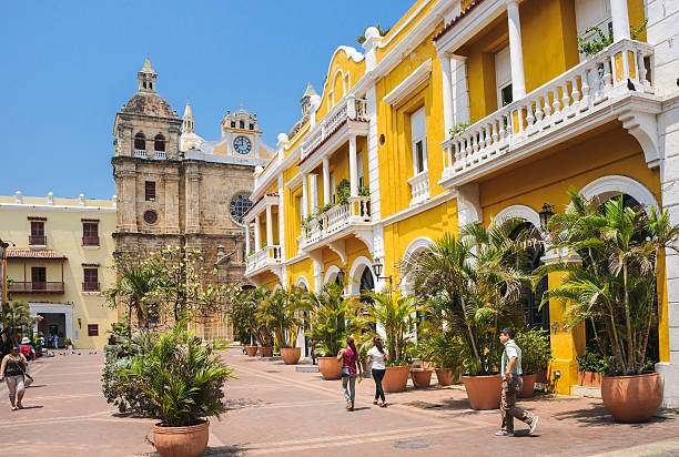 Cartagena, Columbia - March 8, 2013: Tourists, visitors and residents stroll the wide plazas of Cartagena past shops in the colorful old buildings accented by potted palm trees.