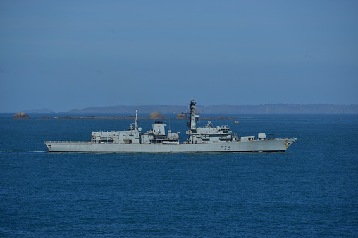 Jersey, U.K.- March 5, 2015: The British royal Naval frigate the HMS 'Portland,' patrolling Channel Island waters, to control over fishing and drug trafficking with the island of Sark on the horizon.