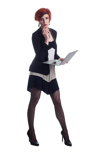 Red haired business woman checks laptop wearing heels and blazer stock photo