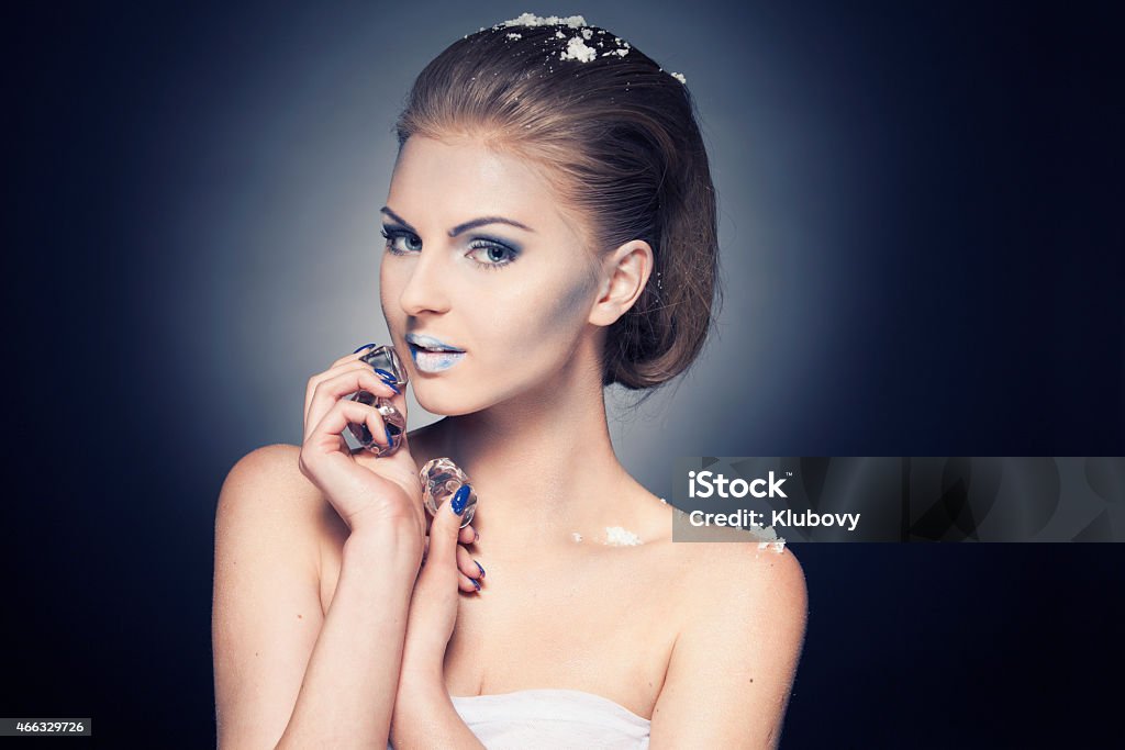 Beautiful woman with cold make-up Portrait of a beautiful young blonde woman with cold make-up and snow on her hair and shoulders. She is holding ice cubes in her hand. Isolated on dark background. 20-29 Years Stock Photo
