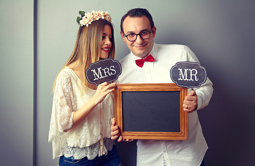 Young couple showing board in front of the gray wall. Board is empty and ready for text or message.