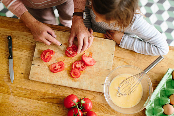 senior frau hacken tomaten mit ihrer enkelin in der küche - hacken essenszubereitung stock-fotos und bilder