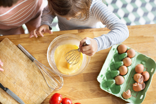 Top view of young girl whipping eggs in a bowl with a wire whisk in kitchen