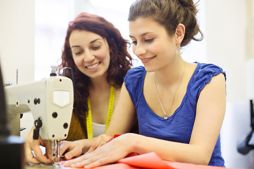 Fashion designer with assistant sewing a dress.. Two young tailors working on a new design inside their fabric shop.