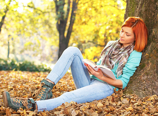 istock Young woman reading a book in nature 466336755