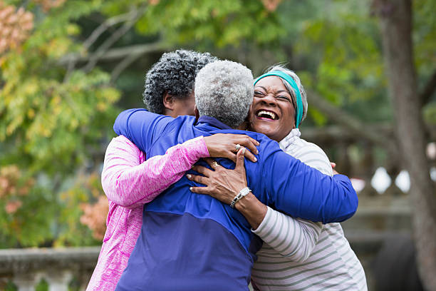 Three seniors hugging Three senior African American women at the park, hugging.  They are best friends excited to see each other. One woman has her eyes closed, with a big smile on her face. family reunion stock pictures, royalty-free photos & images