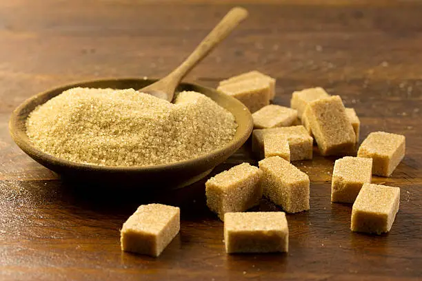 brown sugar in a wooden bowl and sugar cubes on a wooden table