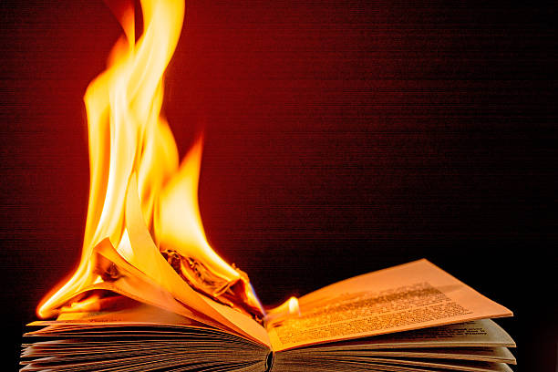 Burning book engulfed in brilliant  flames-  black background. The photo features a burning book engulfed in brilliant orange, yellow, and red flames. Some of the pages are now dark gray and turning to ash. The flame is spreading to he right side of the book. The background is a black color and slightly lit up from the color of the flame. book burning photos stock pictures, royalty-free photos & images