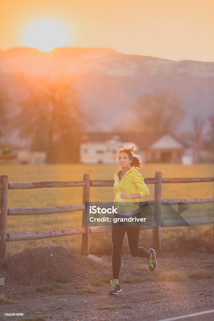 Young Woman in Her 20s Running at Dawn or Dusk Beautiful young mixed race woman on her early morning run on a country road in perfect weather.  Woman has African and Caucasian ethnicity. 2015 Stock Photo