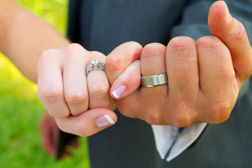 Bride and groom with their hands together and their pinky fingers interlocked for this unique color image of their hands and wedding rings.