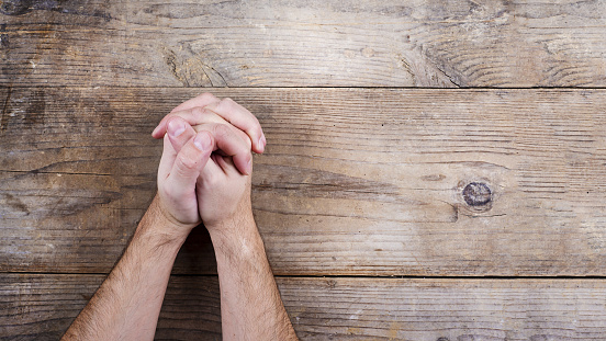 Hands of praying young man on a wooden desk background.