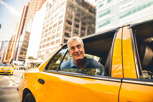 Mature man get on a taxi typical yellow taxi in New York City. He's sitting on the back seat of the yellow taxi in downtown New York