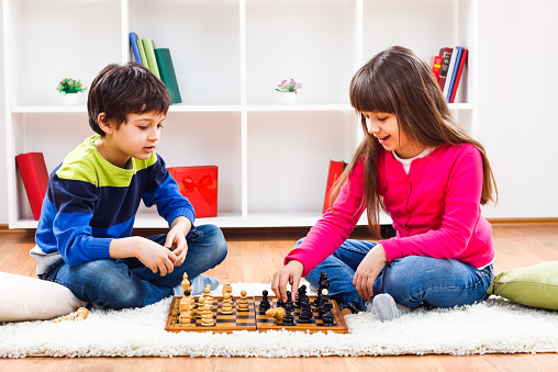 Little boy and little girl are playing chess at home.