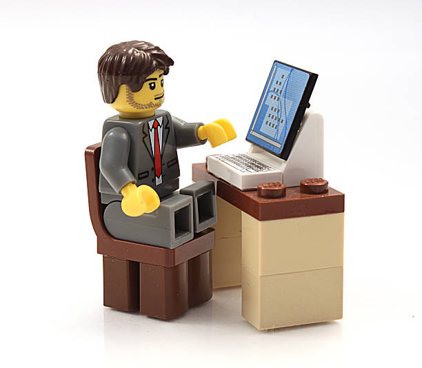 Lego Businessman at his computer Colorado, USA - March 12, 2015: Studio shot of Lego businessman sitting at his computer. Legos are a popular line of plastic construction toys manufactured by The Lego Group, a company based in Denmark. lego stock pictures, royalty-free photos & images