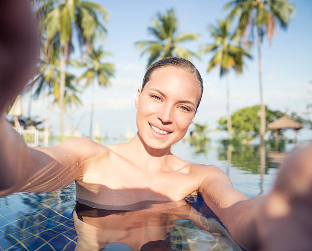 Woman taking a Vacation Selfie in the pool with palm trees in back. High Quality.