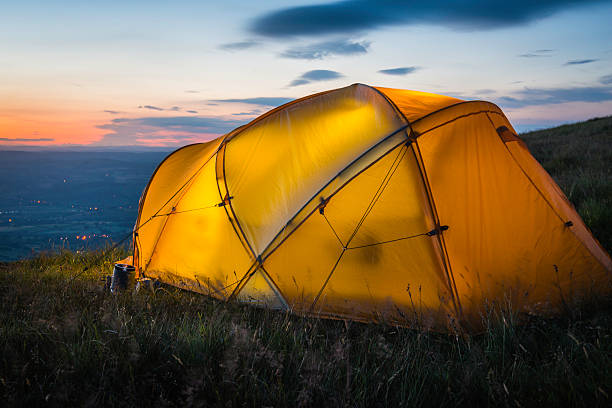 istock Tent illuminated at sunset on mountain overlooking lights in valley 466372946