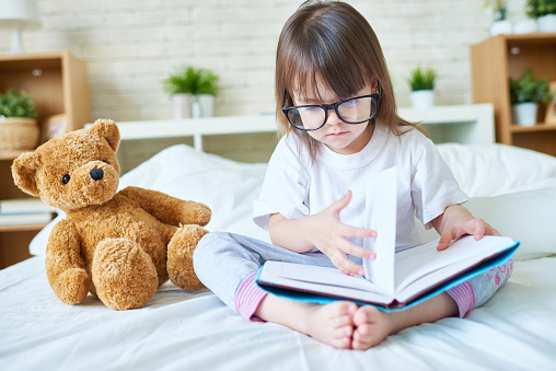 Cute little girl sitting on bed and flicking through a book