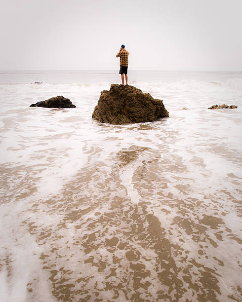 man standing on a rock at el matador beach in malibu, california.  vertical composition.