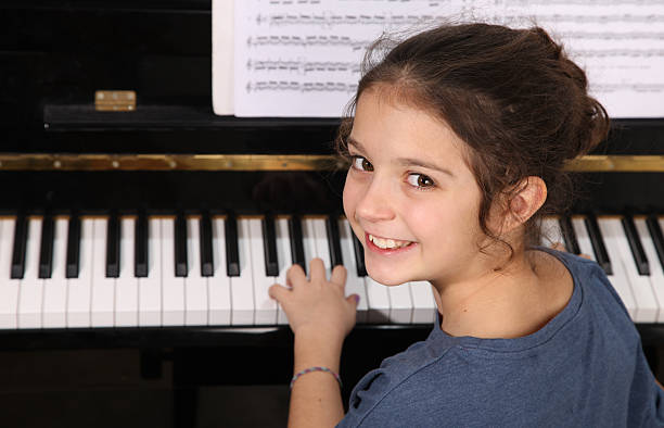 Piano lesson Young girl seated in front of a piano keyboard piano stock pictures, royalty-free photos & images