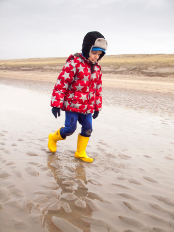 small boy in winter clothing and rubber boots paddling in a tide pool on a winter beach