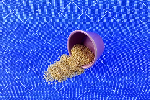 Sesame seeds awoke from a small purple cup on a blue background