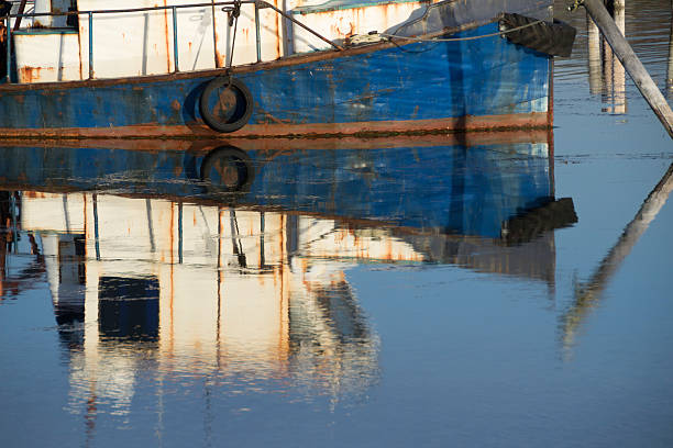 Rusted Blue Hull of Fishing Boat Reflecting in Water stock photo