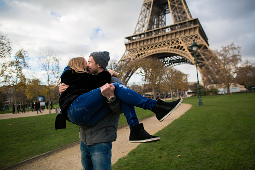 Happy smiling couple kissing and taking selfie photo in front of Eiffel Tower in Paris while traveling across France