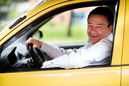 Happy taxi driver driving a car and smiling