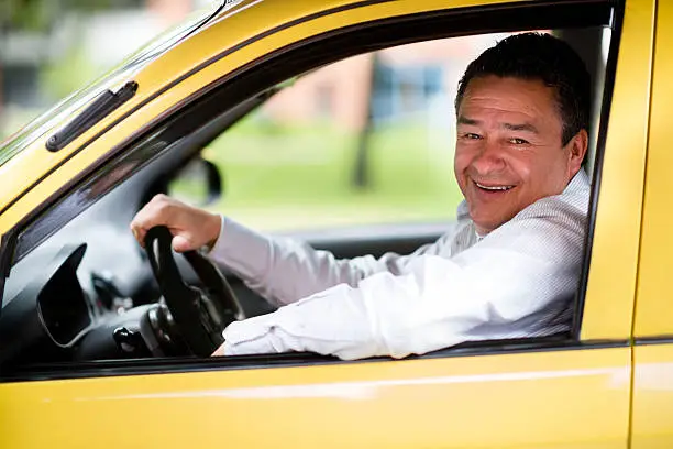 Happy taxi driver driving a car and smiling
