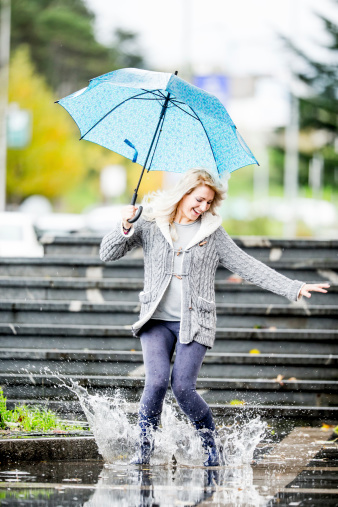 Young woman walking in the city on a rainy day. Jumping in a puddle.