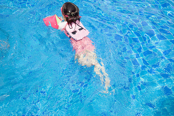 A little girl wearing floating board and water wings learning how to swim.