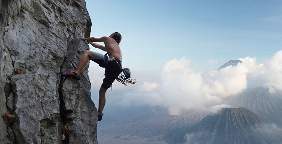 Young man climbing natural rocky wall with volcanoes on the background