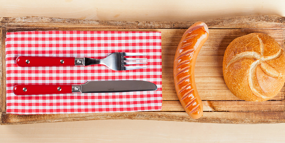 Grilled Sausage with Roll and Cutlery on Wood Plate