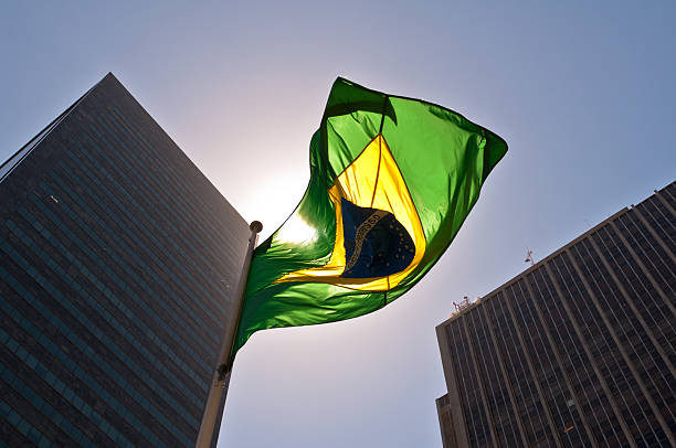A Brazilian flag in front of skyscrapers Brazilian National Flag against Skyscrapers by Sunset. democracy stock pictures, royalty-free photos & images
