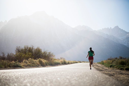 Female athlete, endurance running on a endless road with mountains in the back ground 