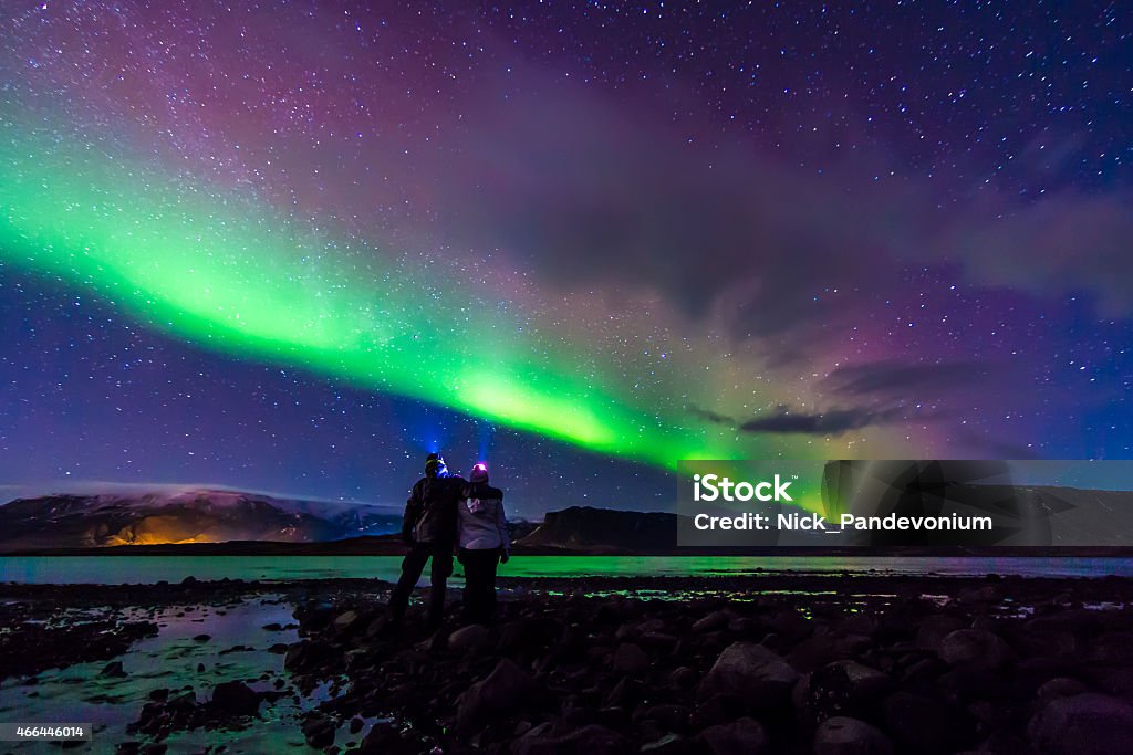 Young Couple hugged under Northern lights Aurora Borealis in Iceland Young adventurist couple hugged while gazing in the dark night sky under the spectacular celestial lights Aurora Borealis, which makes Iceland popular spot for tourist willing to witness one of the greatest natural phenomenon. Shot with Canon EOS, wide angle lens, f2.8, long exposure. Aurora Borealis Stock Photo